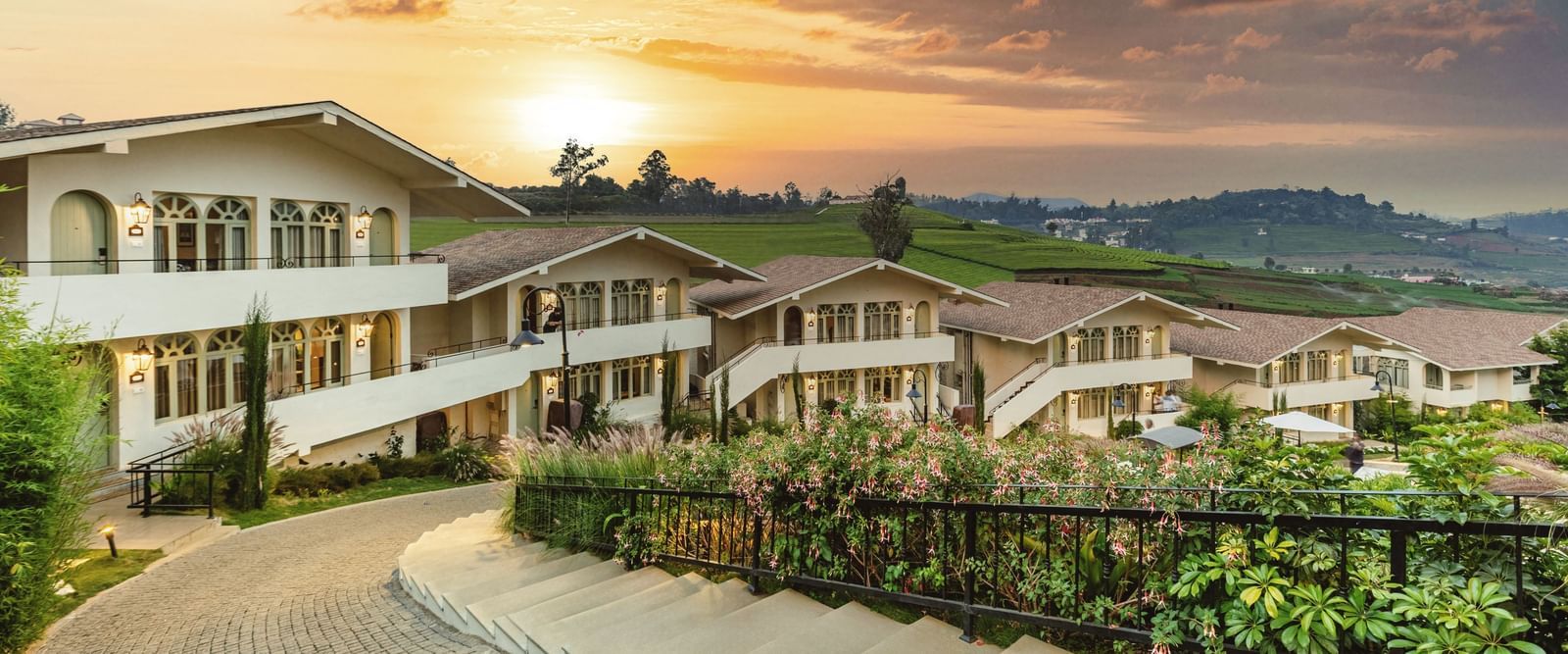 Walkway weaving through Mango Hill Shola, Ooty, flanked by resort buildings and landscaped surroundings.