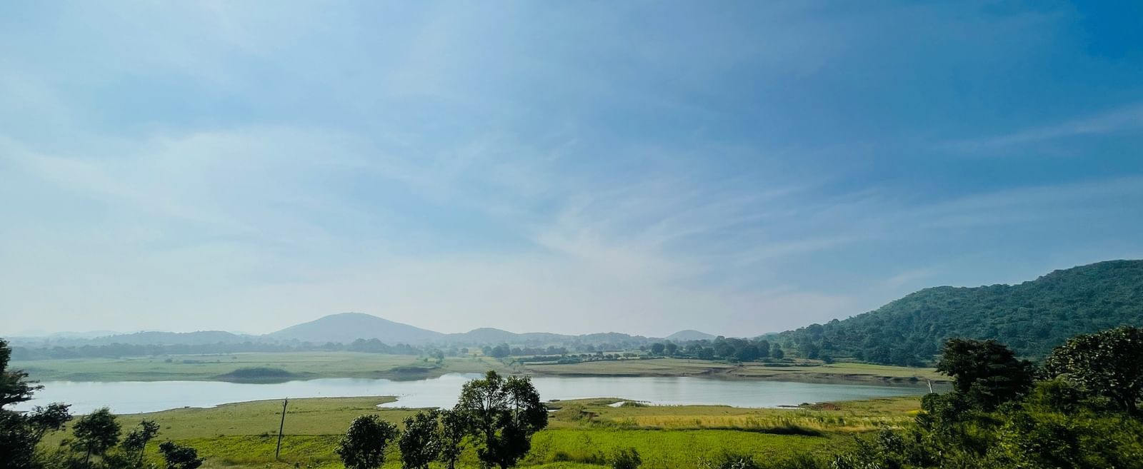 Scenic view of a lush green landscape with a river and hills under a bright blue sky.