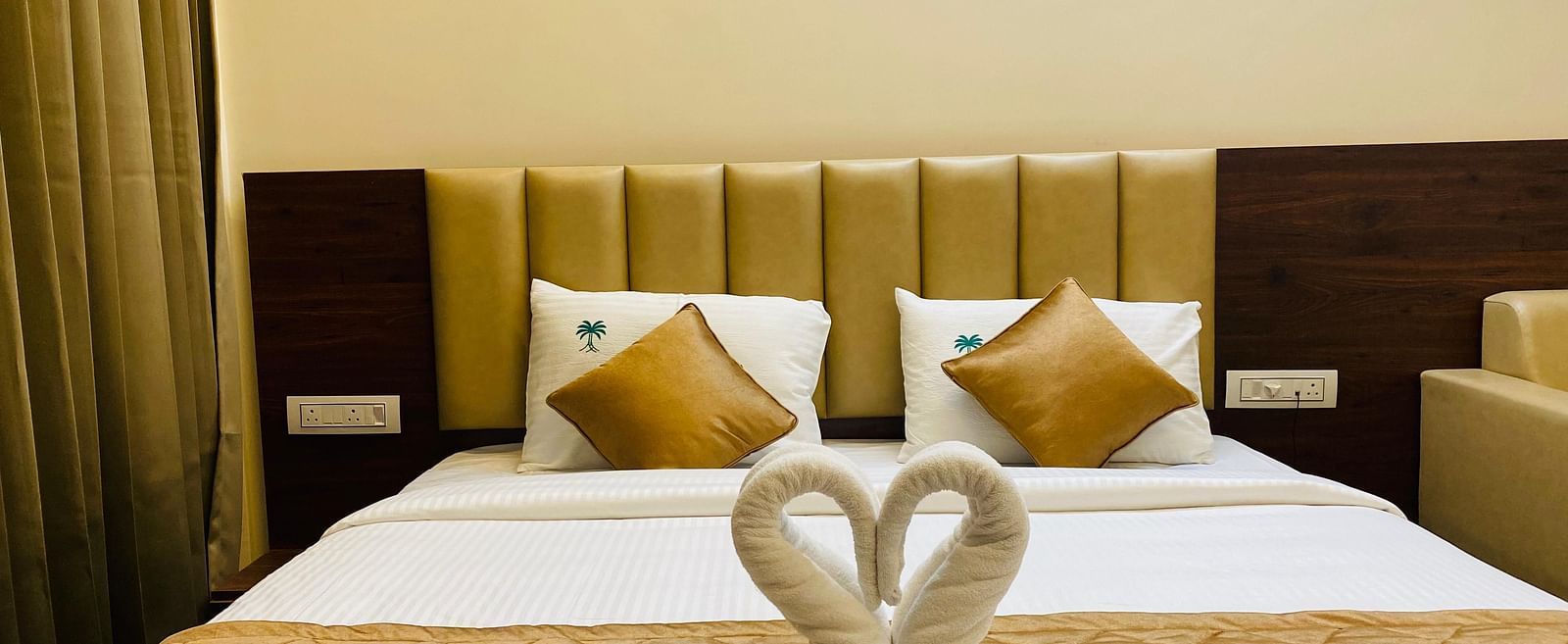 Romantic towel swan decor placed on a neatly arranged bed with golden accents at Hotel Sahara Tree.