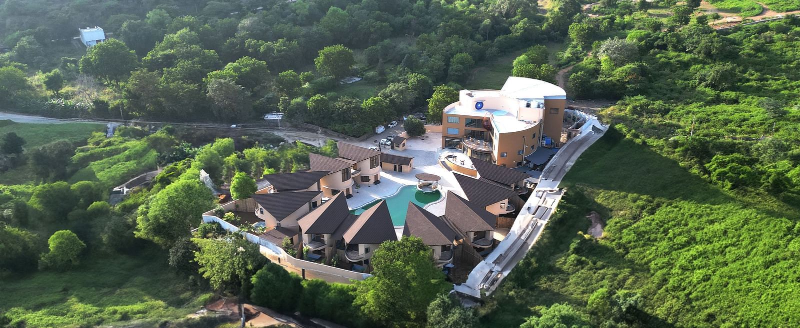 An aerial view of The Qualia Resort Club & Brewery, Udaipur surrounded by lush greenery and hills.