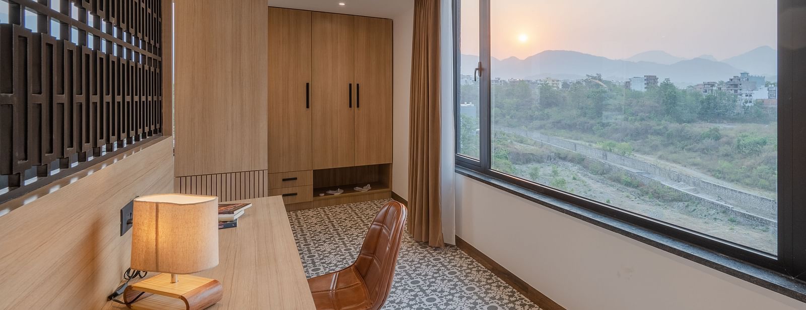 Living area of a suite at Vishranti Hotel, Dehradun featuring a work desk, chair and a large frame window with mountain views.