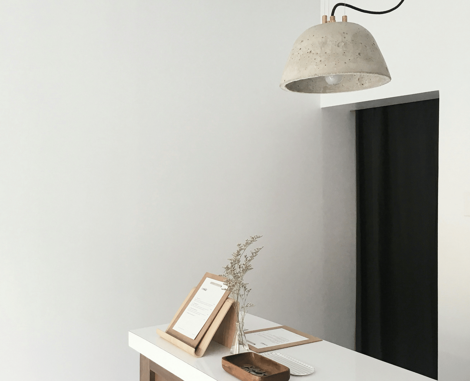 A minimalist interior showing a white wall, a mounted television, a white console table, and a modern pendant lamp.