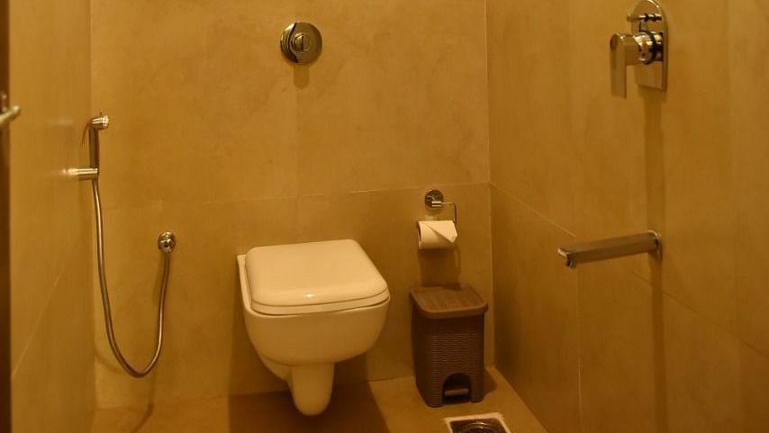 A small bathroom with a toilet, a water heater mounted on the wall, a shower, and a small window.