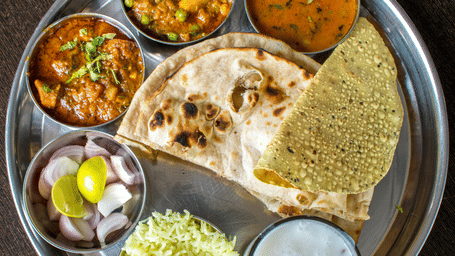 A steel plate with assorted dishes in little bowls surrounding roti and papad