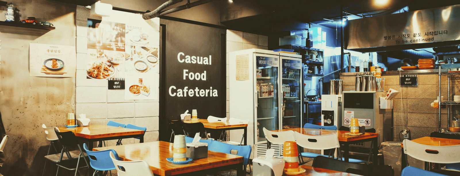 The interior of a modern cafe with tables, chairs, and warm lighting.