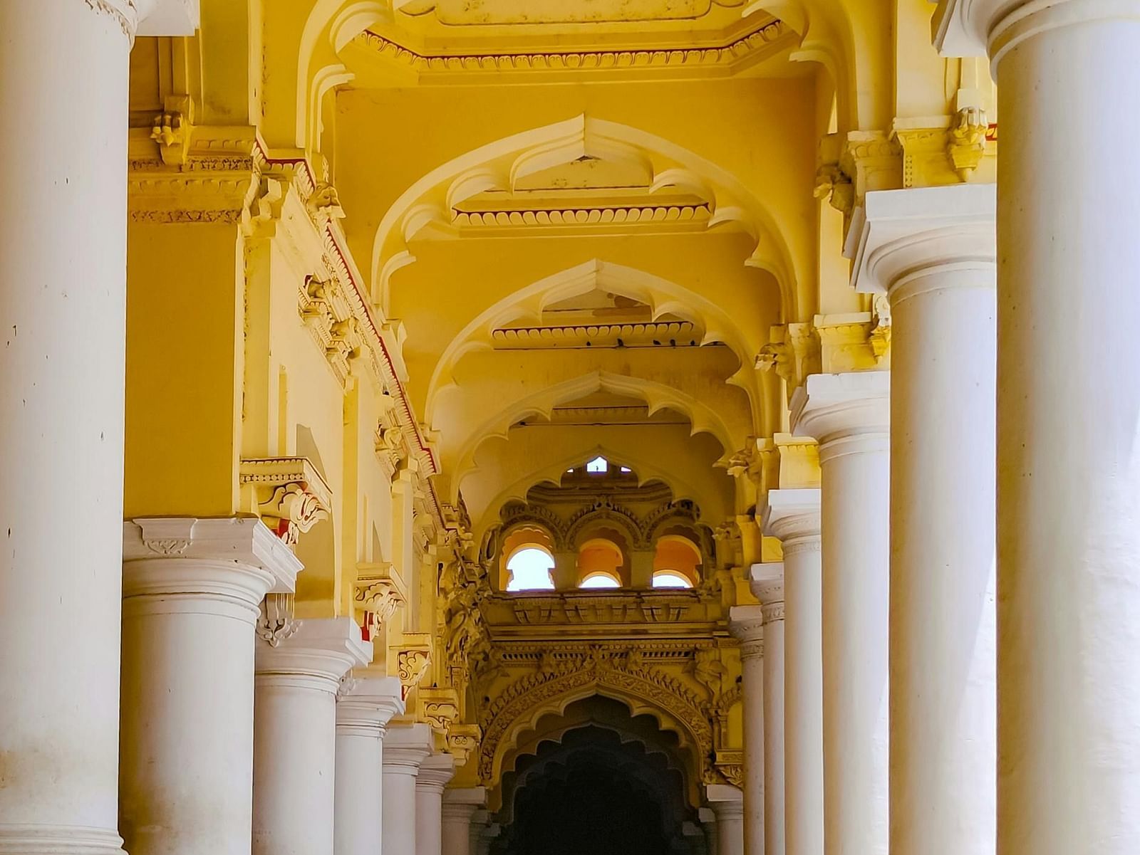 Ornate hallway of Thirumalai Nayakkar Mahal with grand arches and tall pillars.