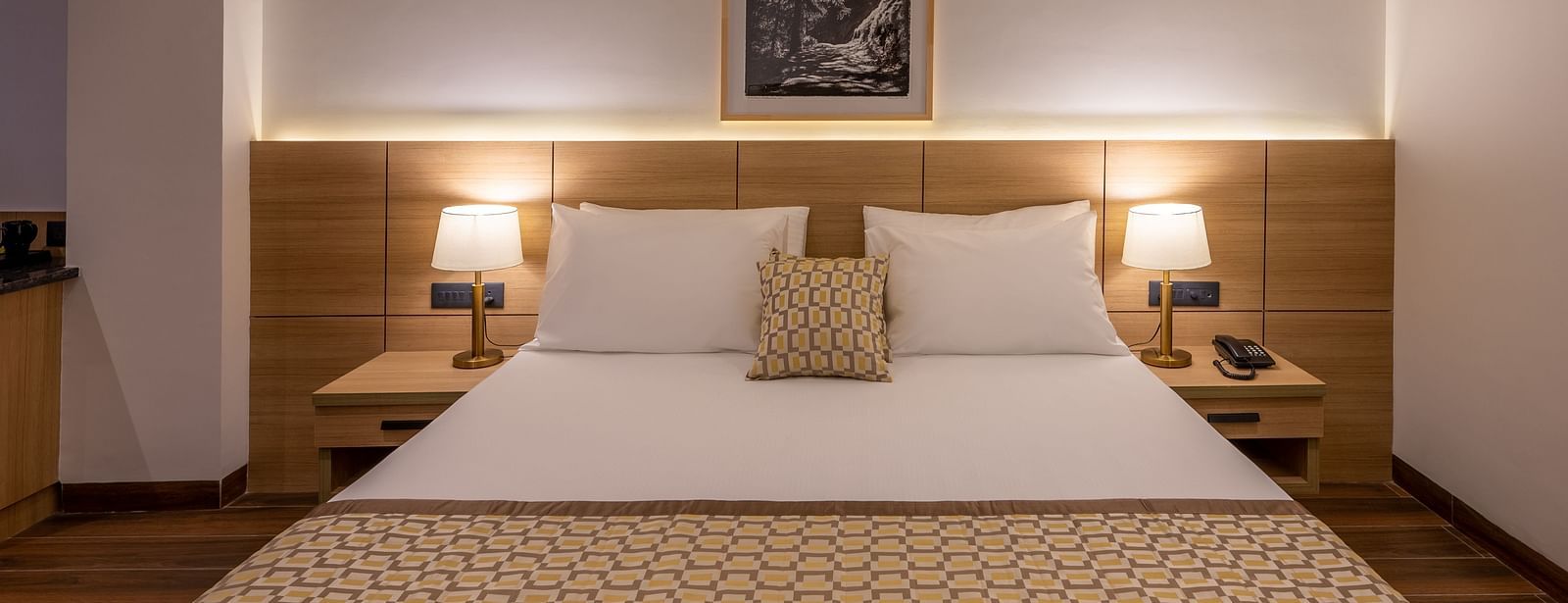 Close up of Premium Room at Vishranti Hotel, Dehradun featuring a king bed with side tables and bed lamps. 