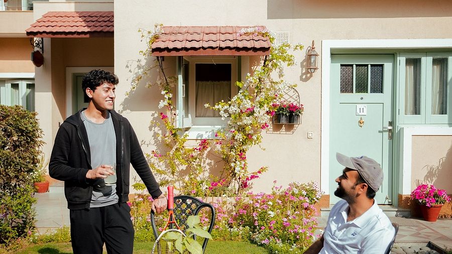 Two men near a round table with drinks in a garden outside a cream-coloured building with balconies and flowering plants | Karma Chalets