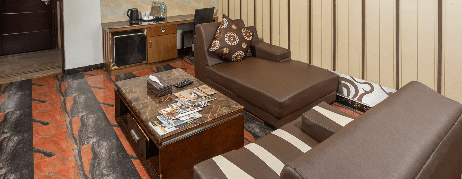 The lounge area of the Premium Room at Parakkat Nature Hotel and Resorts, Munnar featuring comfortable multi-seating sofa, a central coffee table, a small beverage counter, and a vertically-panelled accent wall.