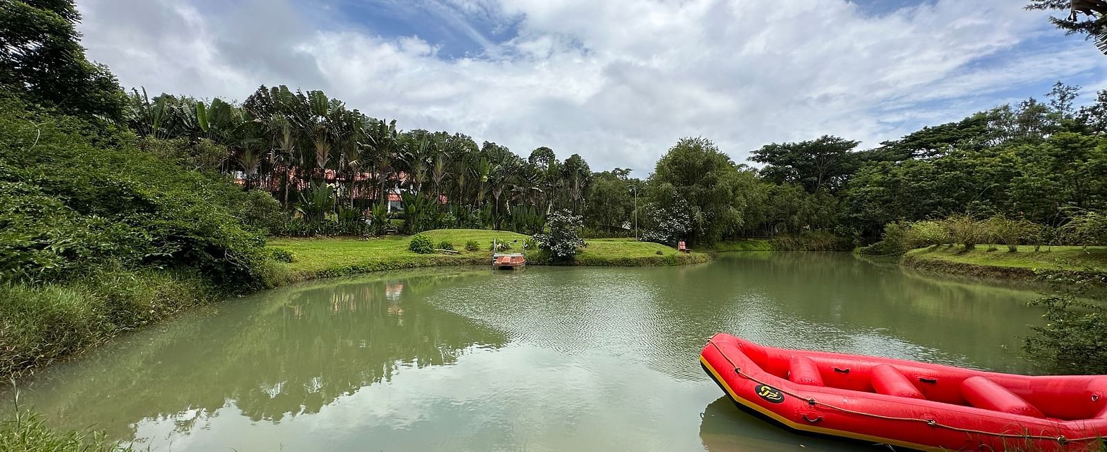 image of a lake with a boat floating in it and trees visible in the distance - Kadkani River Resort, Coorg