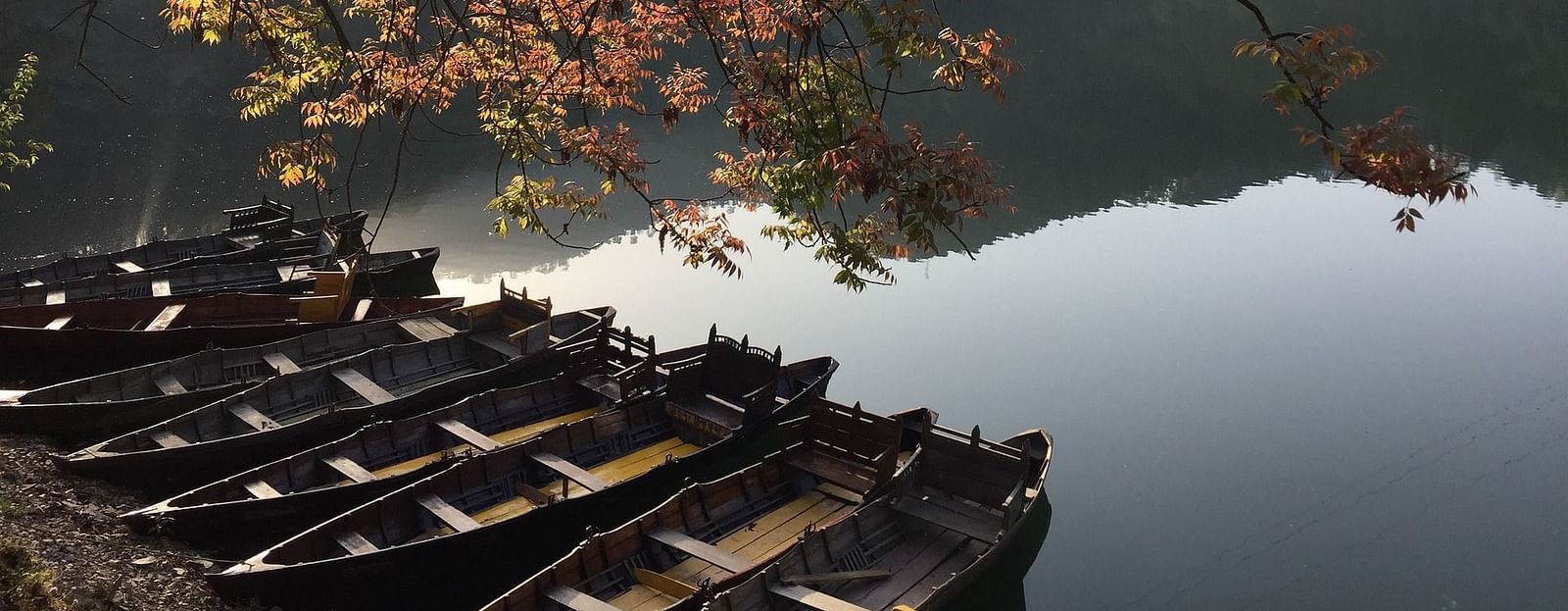 A beautiful side angle shot of a lake, featuring boats lined up along the shore, with serene water reflecting the surroundings.