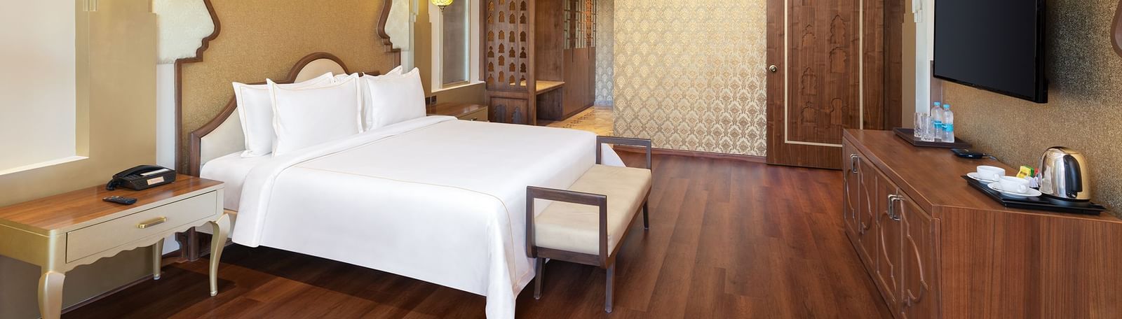 A sophisticated bedroom with wooden floors, golden accents, and plush white bedding – Kaldan Samudra, one of the finest luxury hotels in Mahabalipuram