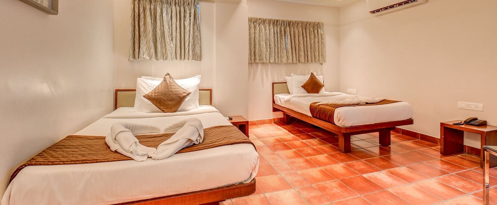 A spacious room at Harigovinda's JNStay with two beds, windows covered by curtains, and a wall-mounted AC
