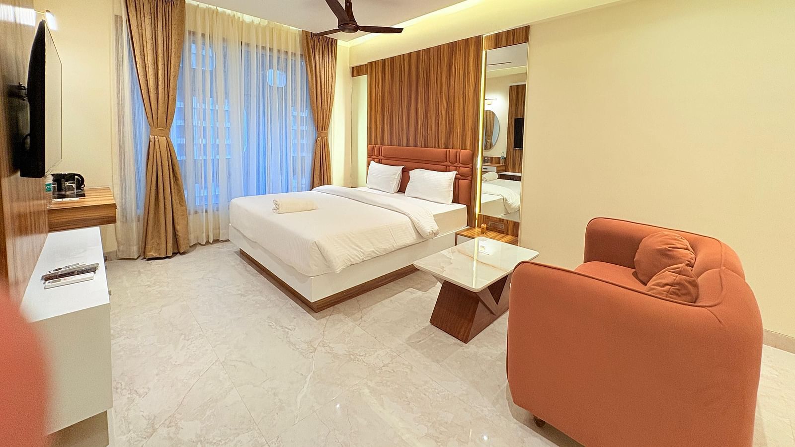 A spacious bedroom featuring a king size bed, a large sofa, and a wall-mounted television at Hotel Mumbai House, Vashi