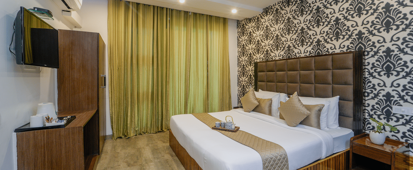 The deluxe room at DLS Whispering Winds showcasing a bed, a bed side table, and a flat screen TV along with other room amenities