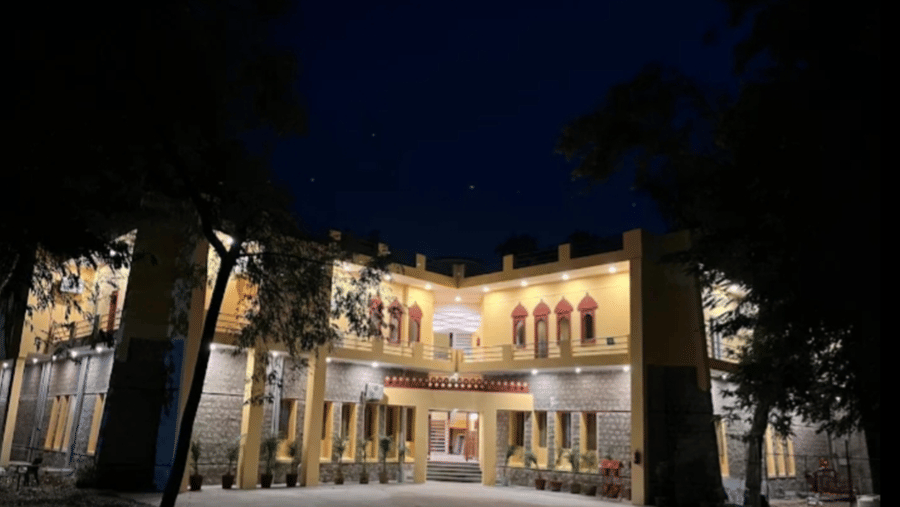 The facade of Estherea Bagh, Ranthambore, is lit up at night, highlighting the stone and yellow walls of the building.