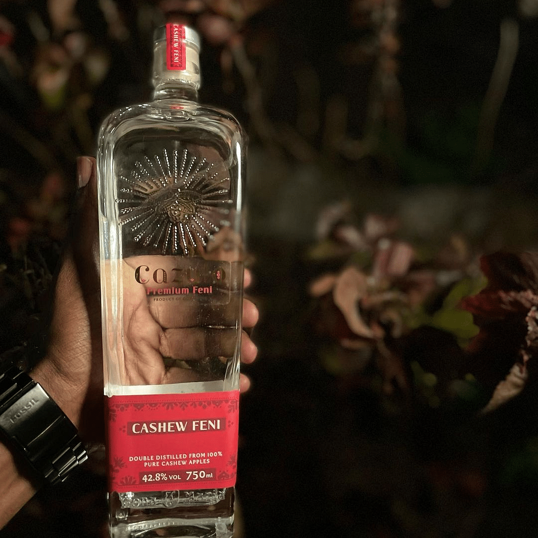 an image of a person holding a glass bottle of cashew feni - Villa in Palms by V Escapes