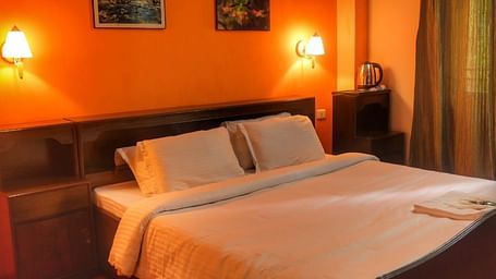 An image of the deluxe room featuring a queen size bed, bed side table, lamps, and painting hung on the wall - Sumitel Chiminda, Pelling