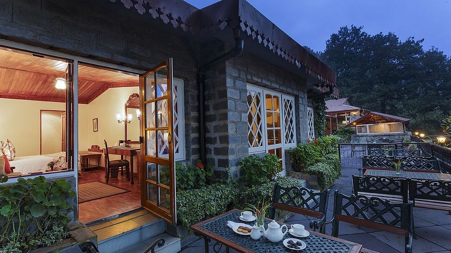 A outer view of the naini retreat, nainital, with a stone exterior and a wooden door leading to a spacious living room with a dining table.,Outside.