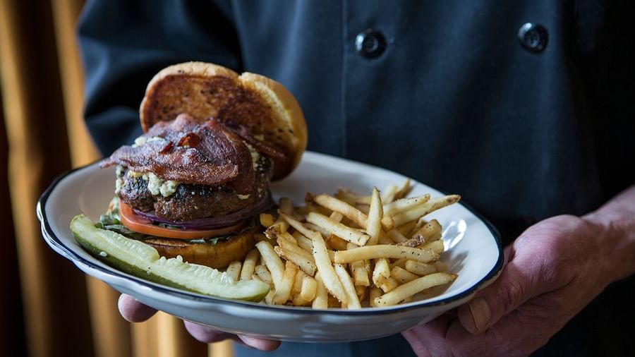 A chef presents a burger with bacon and fries, a specialty at the Tallman Hotel.