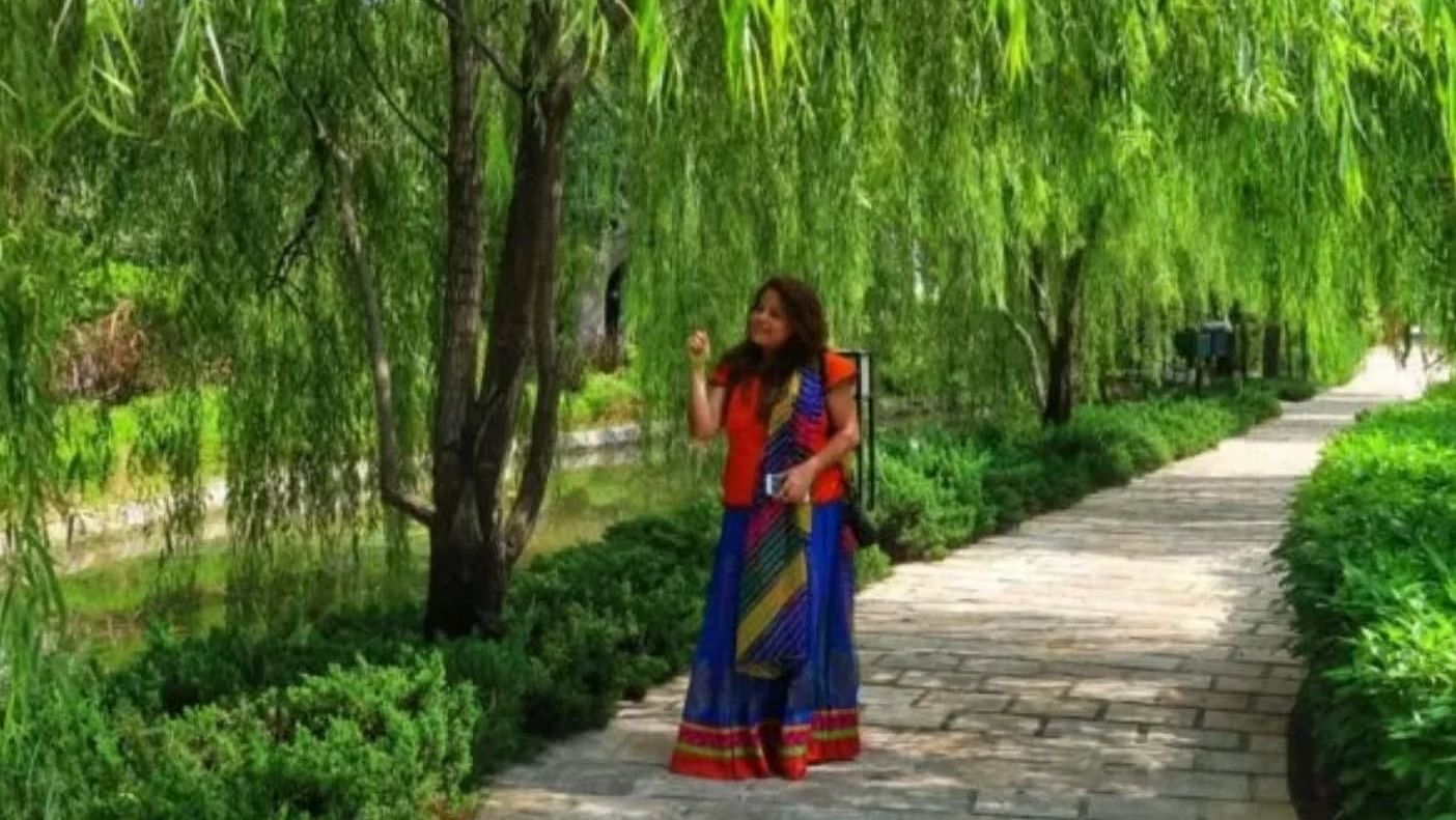 A woman dressed in a saree standing on a pathway surrounded by dense greenery - Ivory Destinations