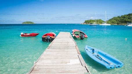 A long shot of a beach with a woodden bridge in between with boats on either side.