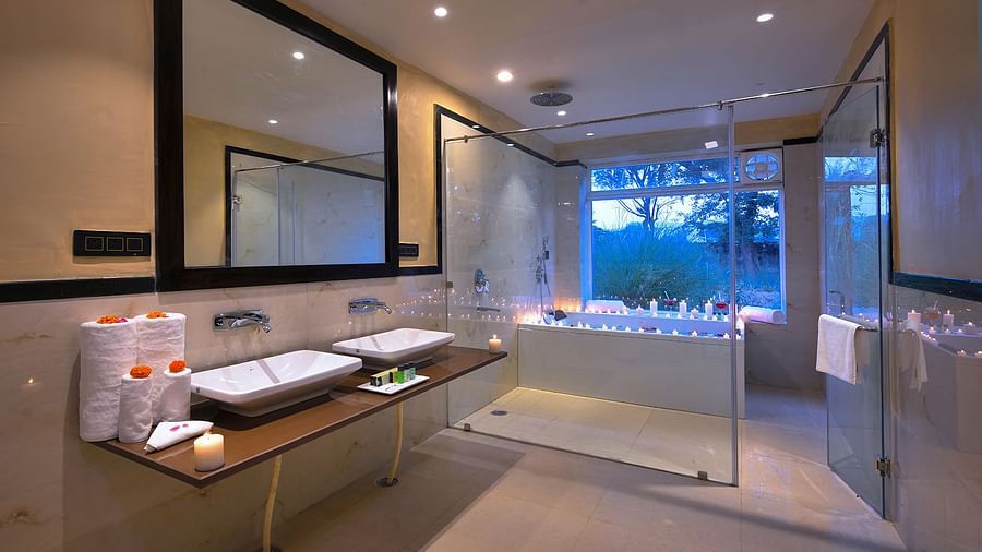 Luxury Suite Cottage with a double vanity, large mirror, glass shower enclosure, candlelit bathtub by a window, and recessed lighting in a bathroom - Singhvilas, Ranthambore