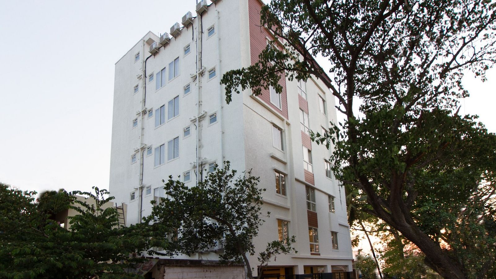 The multi-storey building of Sanctum Suites Whitefield, Bangalore amongst trees under a daytime sky.
