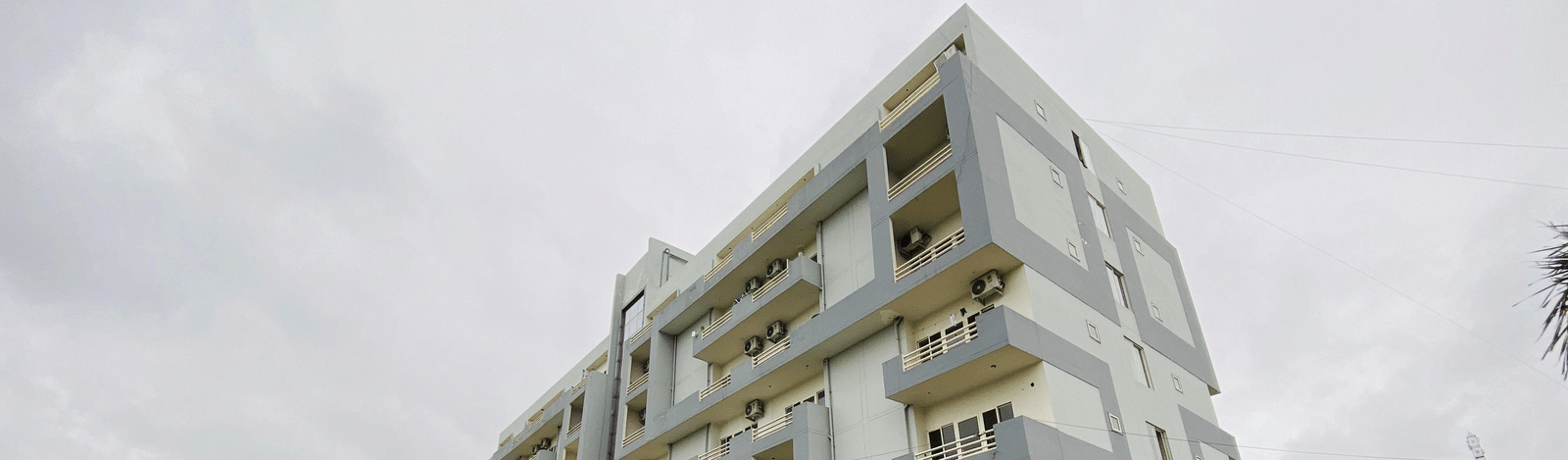 An exterior shot of a modern, multi-story white building with balconies and angular architecture under a cloudy sky.