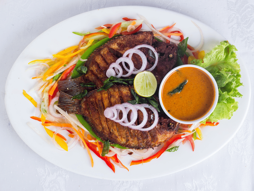 Kerala-style fried fish served with curry, fresh salad, and lime at the restaurant at Abad Brookside Lakkidi, Wayanad.
