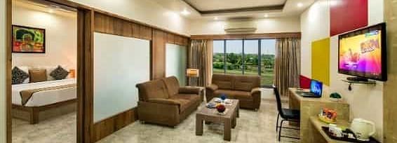 A spacious room including a seating area with sofas, a television, and large windows - Lion Lords Inn Rajula