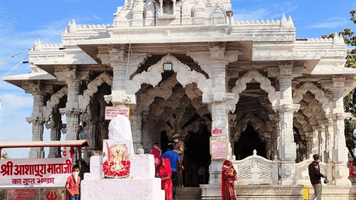 A white marble Jain temple with intricate carvings and arched entryways, set against a bright blue sky.