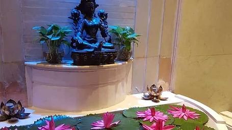 A view of a hindu idol with plants on both sides and lotuses before.