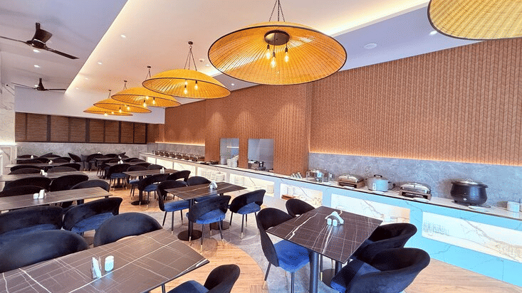 Nautilus restaurant with dining tables, black chairs, and large woven pendant lights at Ocean Palms Goa Resort.