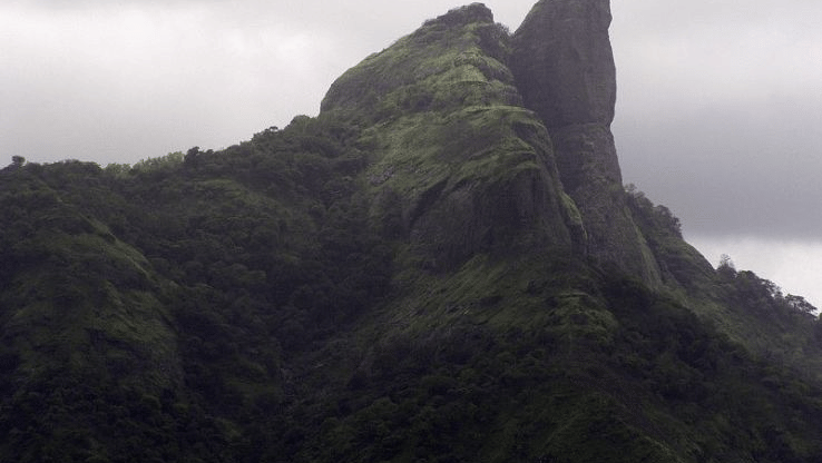 An overview of Duke's Nose in Khandala with trees and greenery on it and overcast skies in the background.