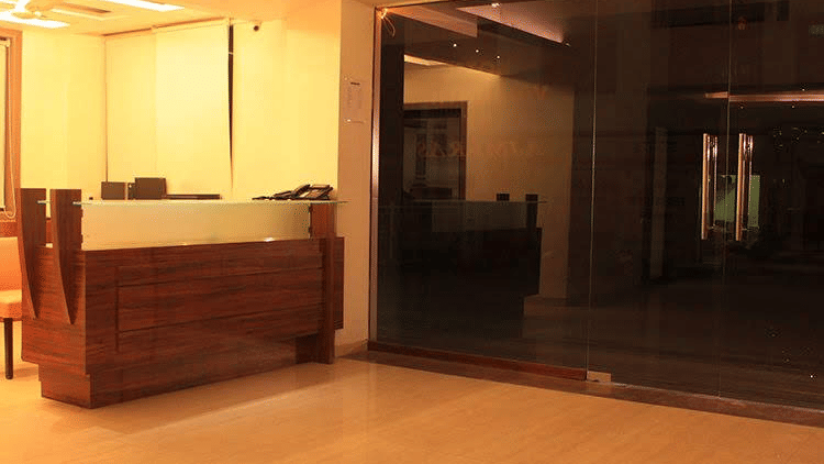 Warmly lit hotel reception lobby showcasing a polished wooden front desk counter and dark glass entrance doors.