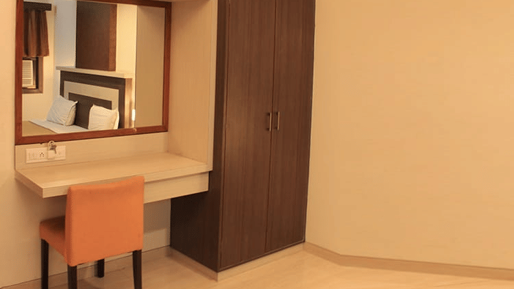 A wooden dressing table with a large mirror, an orange chair, and a matching tall wardrobe in a room corner.