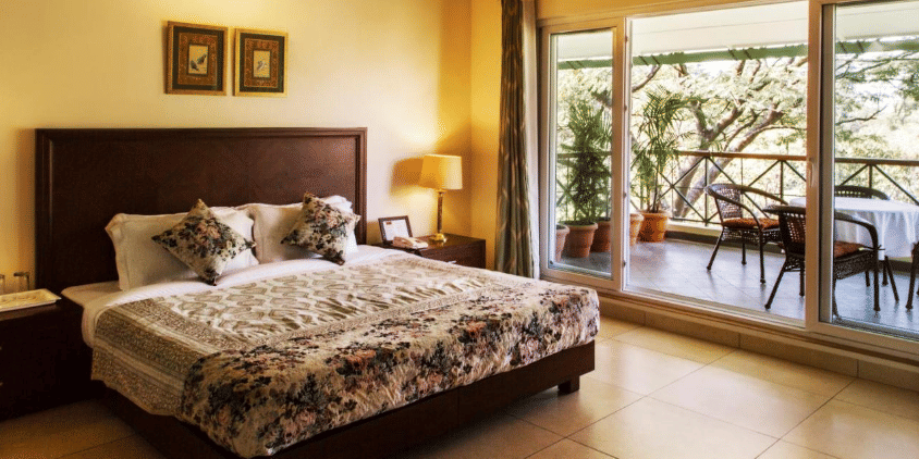 Side angle view of super deluxe room that showcases soft hues of yellow and white along with a balcony overlooking tea gardens - Lamrin Norwood Green, Palampur