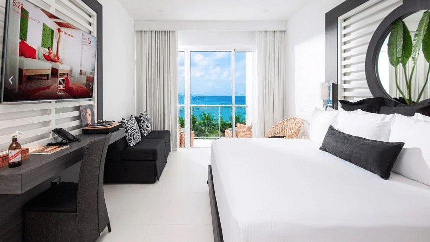 A sea-view room in Jamaica with a large bed, a work desk, a couch and a wall-mounted television - S Hotel Montego Bay, Jamaica