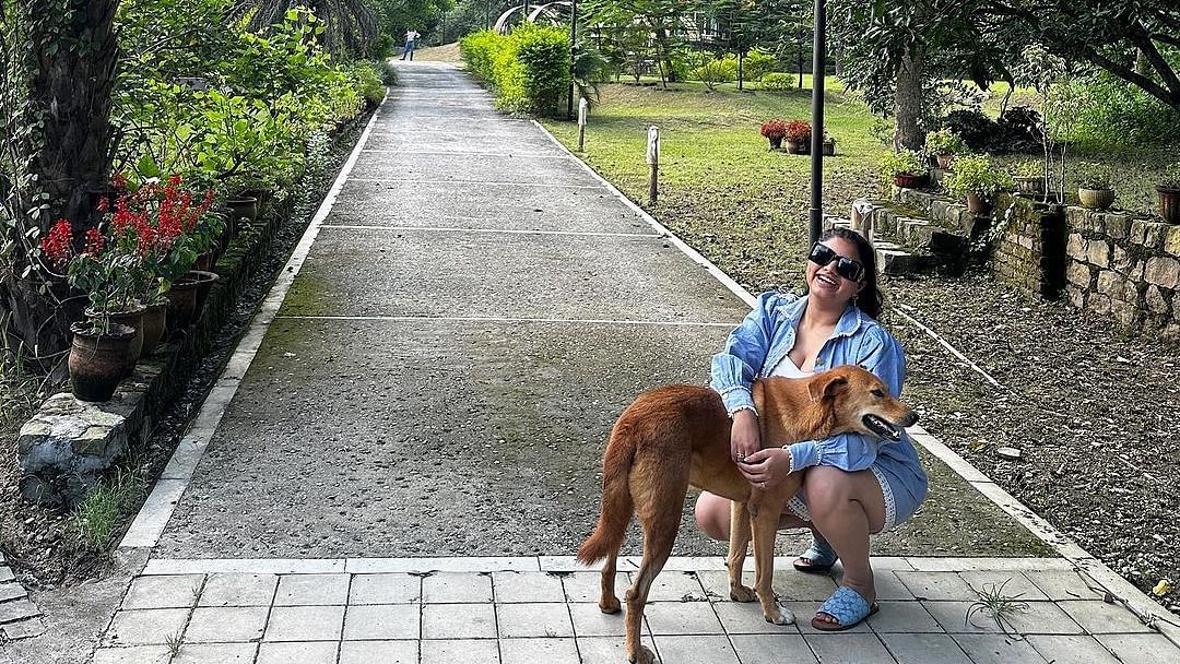 A woman petting a dog on a pathway surrounded by greenery at the Sylvan Retreat, Dehradun.