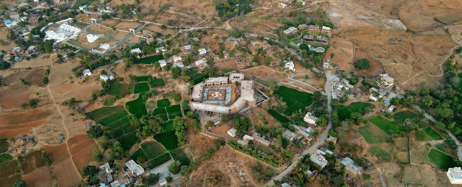 An aerial shot of a small village nestled in a dry, hilly landscape, showing fields and scattered buildings.