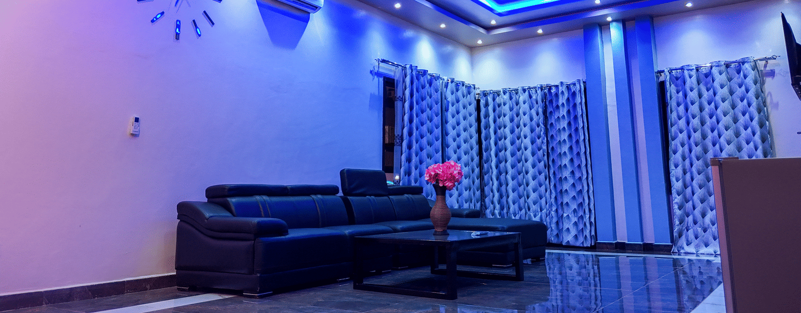 Spacious living room with blue ceiling lights, sofa, and ceiling-to-floor curtains - Luffu Club