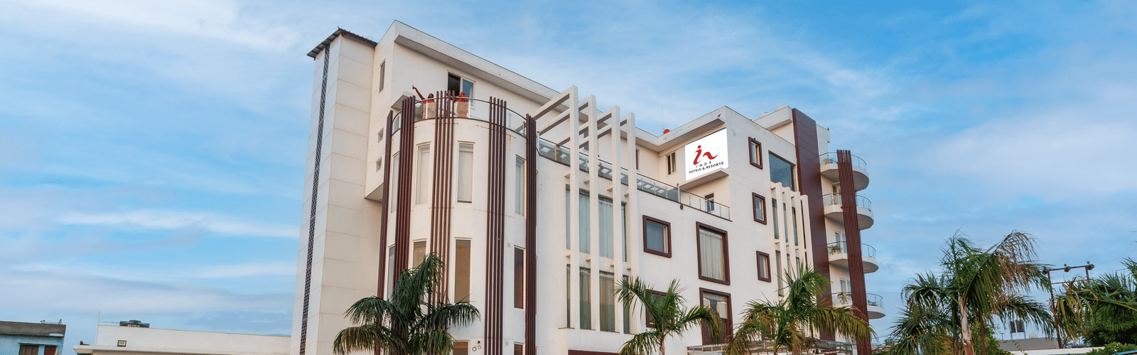 Exterior view of Inde Reva Resorts Rishhikesh with paved driveway, parked car and palm trees.