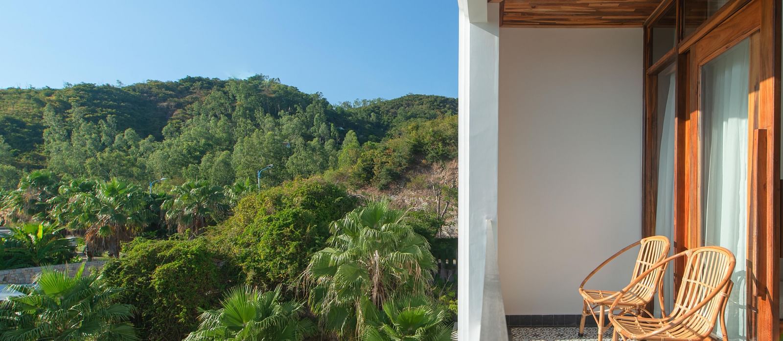 A balcony in one of the rooms at our hotel with a view of lush greenery surrounding it and comfortable chairs to rest upon - Alibu Resort Nha Trang