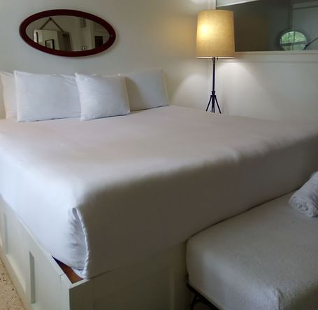 A single bed at Casa Morada with white bedding, a floor lamp, and an oval mirror mounted on the wall above the headboard.