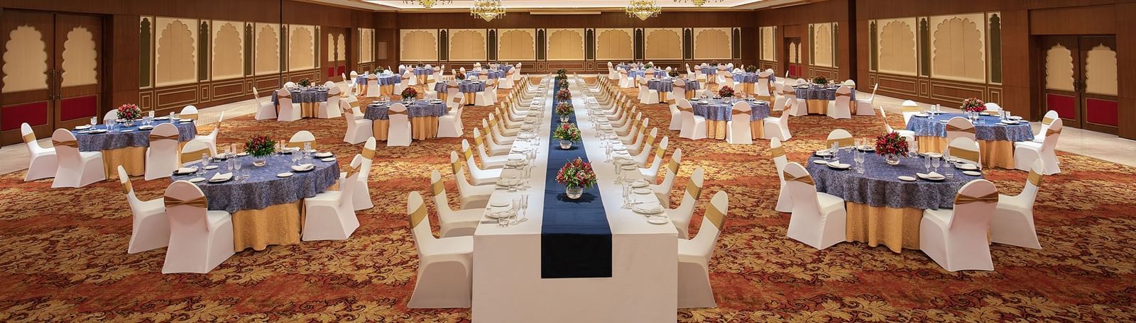 An image of a cosy event hall in Mahabalipuram with long and round tables, chandeliers, and carpeted floors – Kaldan Samudra Palace, a Luxury Wedding Hall in ECR