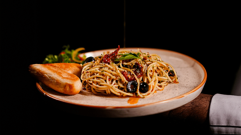 Chef pouring olive oil over a gourmet pasta dish