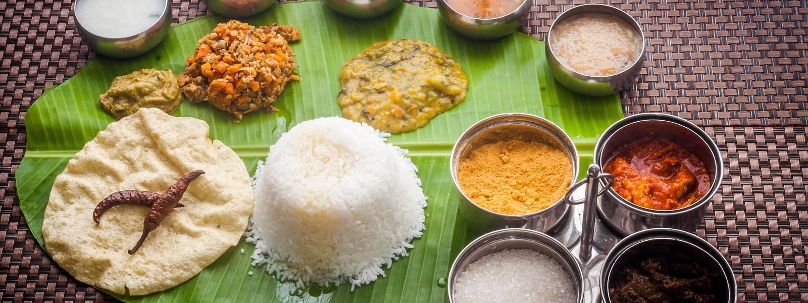 An assortment of South Indian cuisine featuring fluffy rice, a variety of savoury curries, and accompaniments, all ready for a feast.