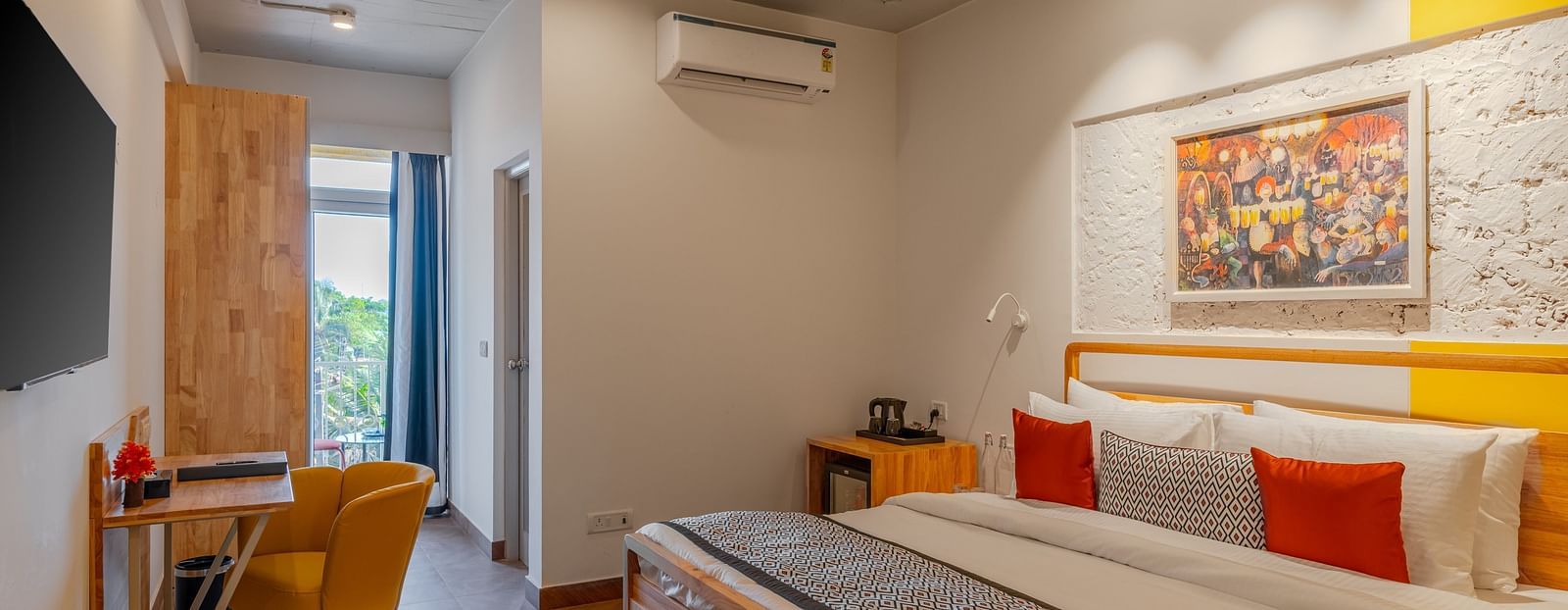 Bright hotel room with, flat TV screen, work desk and chair, vibrant art on the wall, and an access to the balcony at Bedzzz Xclusiv Morjim, Goa