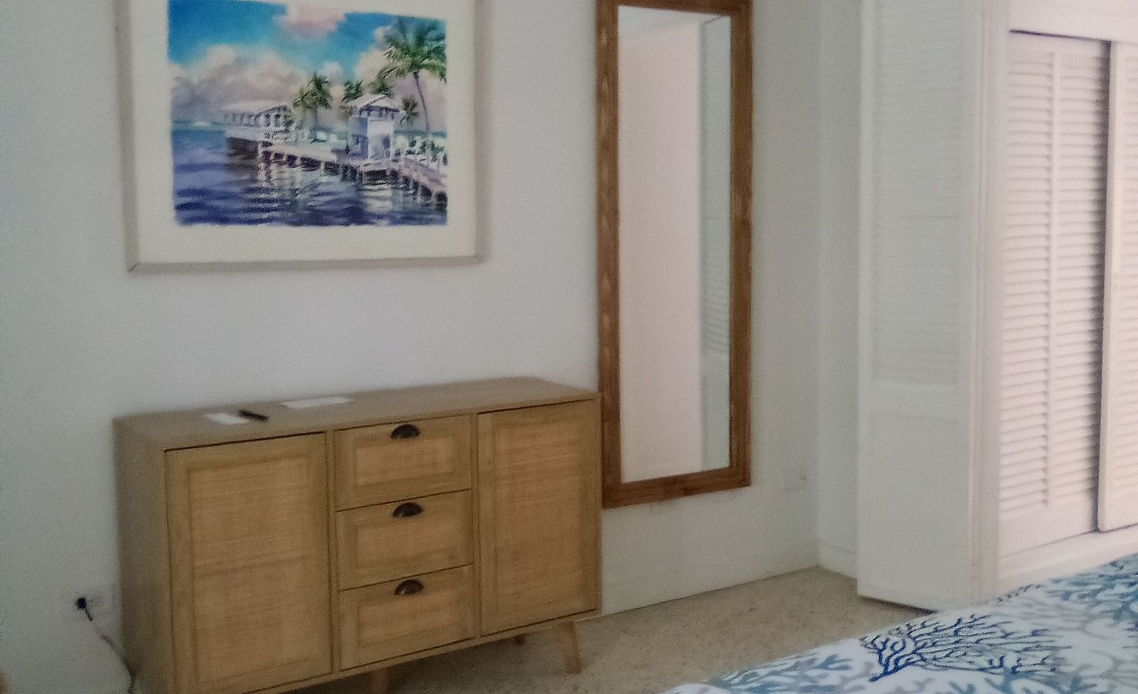 Bedroom at Casa Morada with a wooden dresser, framed wall art, and part of a bed with a patterned blue cover.